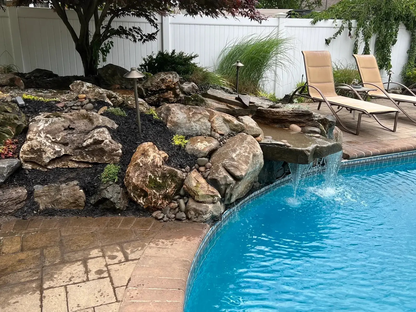 Poolscape with stone terrace and rock waterfall spilling into a pool in Nassau County