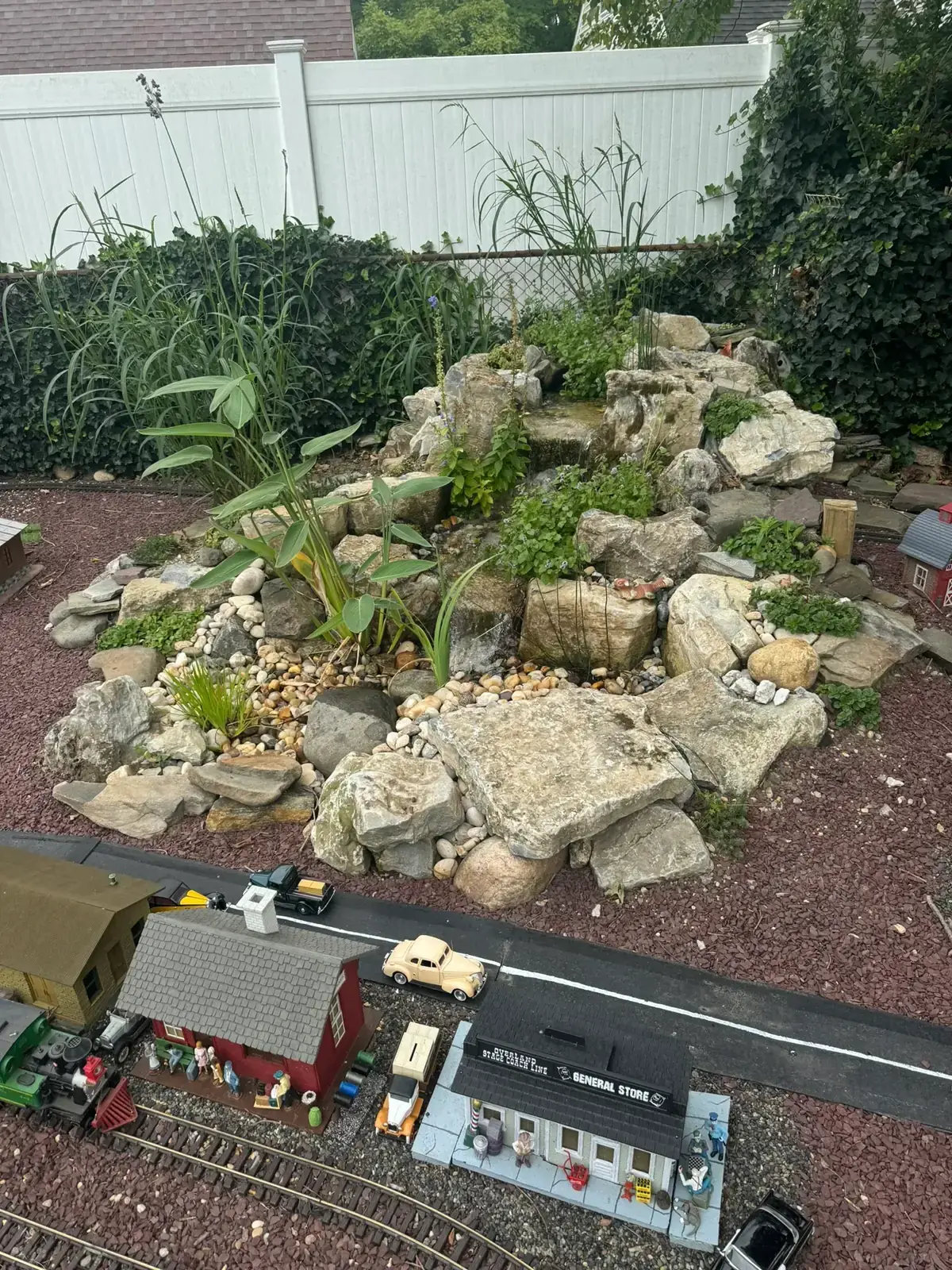 Pondless waterfall over stacked stone forming the backdrop of an outdoor model train garden on Long Island